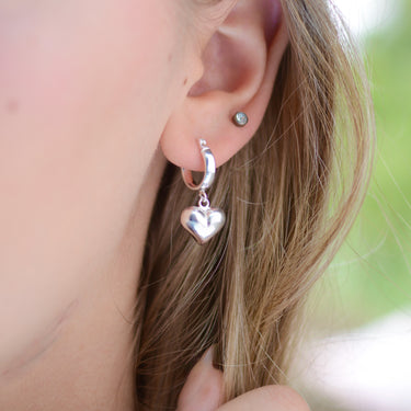 Sterling Silver Huggie with puffed heart charm shown close up on model