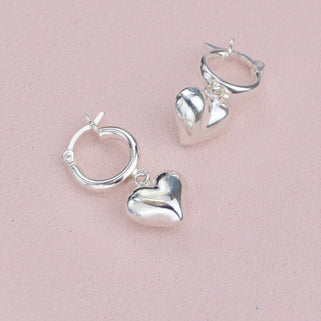 Sterling Silver Huggie with puffed heart charm shown close up .