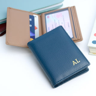 Light navy card holder with gold monongram initials and taupe wallet open at rear.