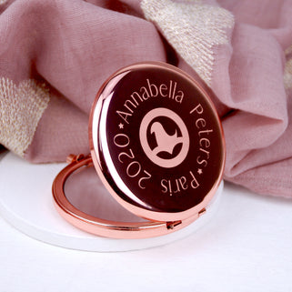 Rose gold compact mirror with personalised logo in the centre and text engraved around the outside, shown in close up with model.