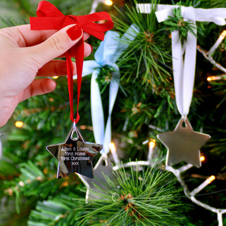 Christmas Star Tree Decoration with Personalised message "Adam & Louise first Home First Christmas xxx" engraved on the front with red ribbon shown in close up shot held in front of Christmas tree