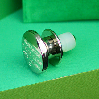 Christmas Wishes Wine Bottle Stopper with Personalised message "Mistletoe & Wine Time Love James X" engraved on top of stopper shown in close up shot on green background