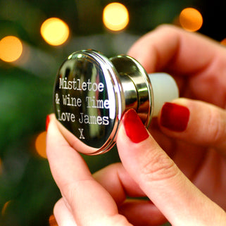 Christmas Wishes Wine Bottle Stopper with Personalised message "Mistletoe & Wine Time Love James X" engraved on top of stopper shown in close up shot held sideways by model